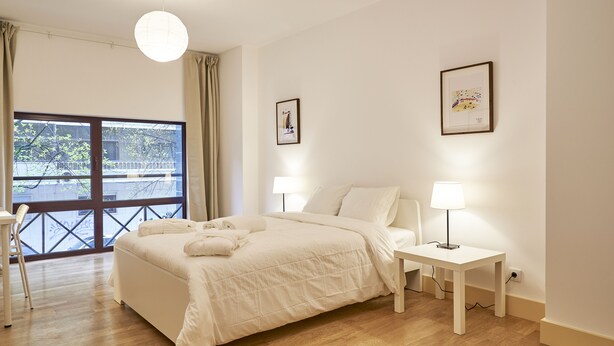 A bedroom with a large bed, two bedside lamps, a window with curtains, and two framed pictures on the wall. - Campo Pequeno Avenida (Lisbon)