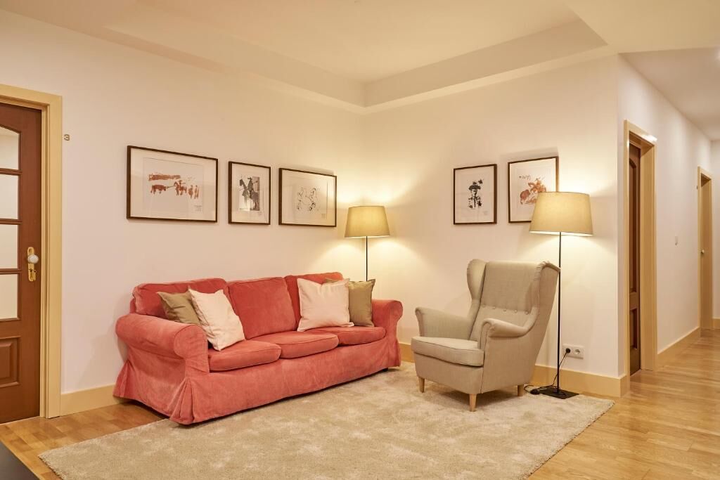 A room with a red sofa, a beige armchair, and a floor lamp. There are framed pictures on the wall.