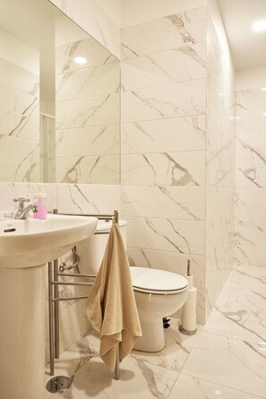 Een badkamer met een betegelde wand van marmer, een wastafel met zeepdispenser, een handdoek aan een rek en een toilet.