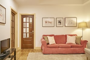 Een woonkamer met een houten deur, een roze bank, een flatscreen televisie en kunstwerken in lijsten aan de muur.