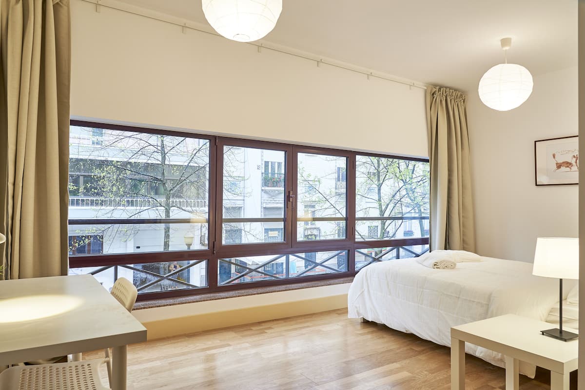 Een hotelkamer met een groot raam, een bed, een nachtkastje en een stoel.