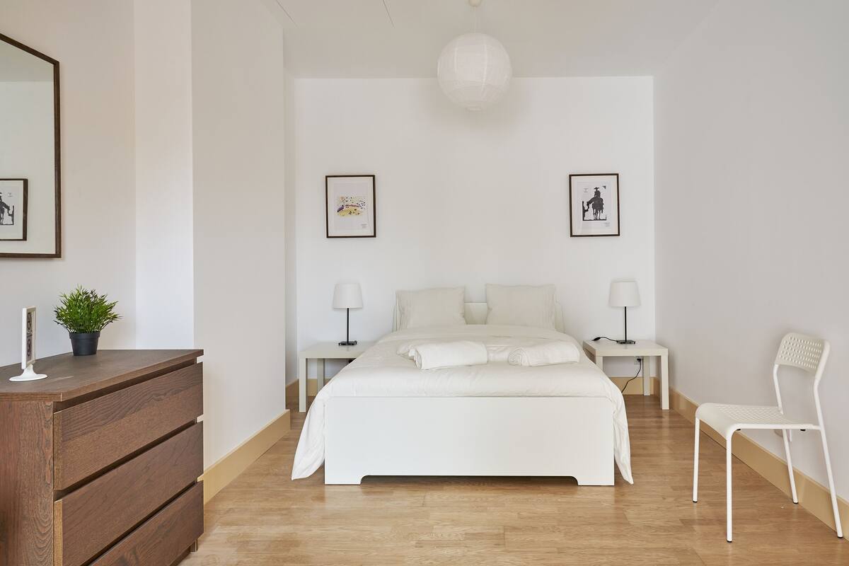 Een slaapkamer met een groot bed, een kaptafel, twee nachtkastjes met lampen, en ingekaderde foto's aan de muur.