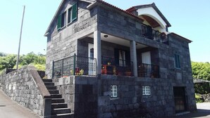 A two-story stone building with a balcony, a staircase leading to the entrance, and a small porch area. - Great Tranquility Holiday Home (S.Roque do Pico)
