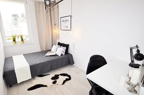 A modern bedroom with a bed, a desk, and a chair. There is a window with curtains and a sign on the wall.