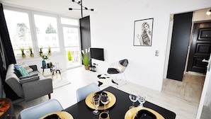 Un salon moderne avec un coin repas, de grandes fenêtres et une décoration aux couleurs noir et blanc.