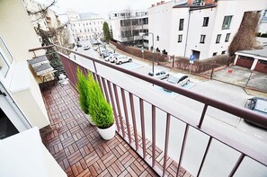 A balcony with a potted plant, a view of parked cars, and a building with multiple windows and balconies.