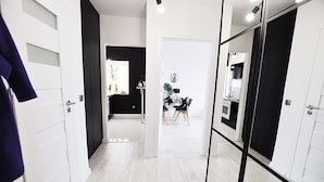 Un couloir mène à une salle à manger avec une table et des chaises, à une cuisine équipée de placards et à une porte dotée d’un miroir.