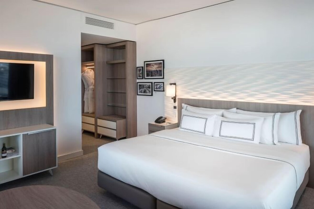 A modern hotel room with a large bed, a TV mounted on the wall, a walk-in closet, and framed pictures on the wall.