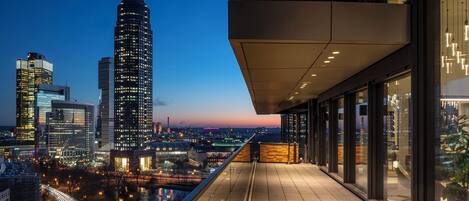 A high-rise building with a distinctive spire, modern architecture, and a view of the cityscape at dusk.