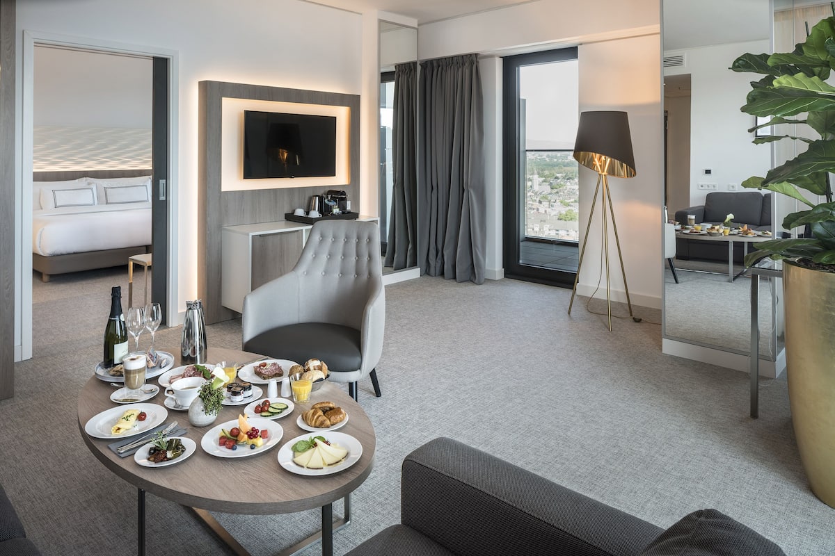 Ein modernes Hotelzimmer mit Essbereich, großem Fenster, Flachbildfernseher und einer großen Topfpflanze.