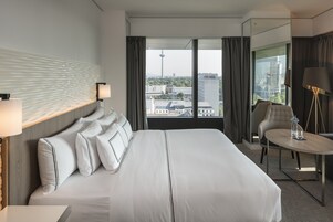 Una habitación de hotel con una cama grande, vistas de la ciudad y una mesita con lámpara.