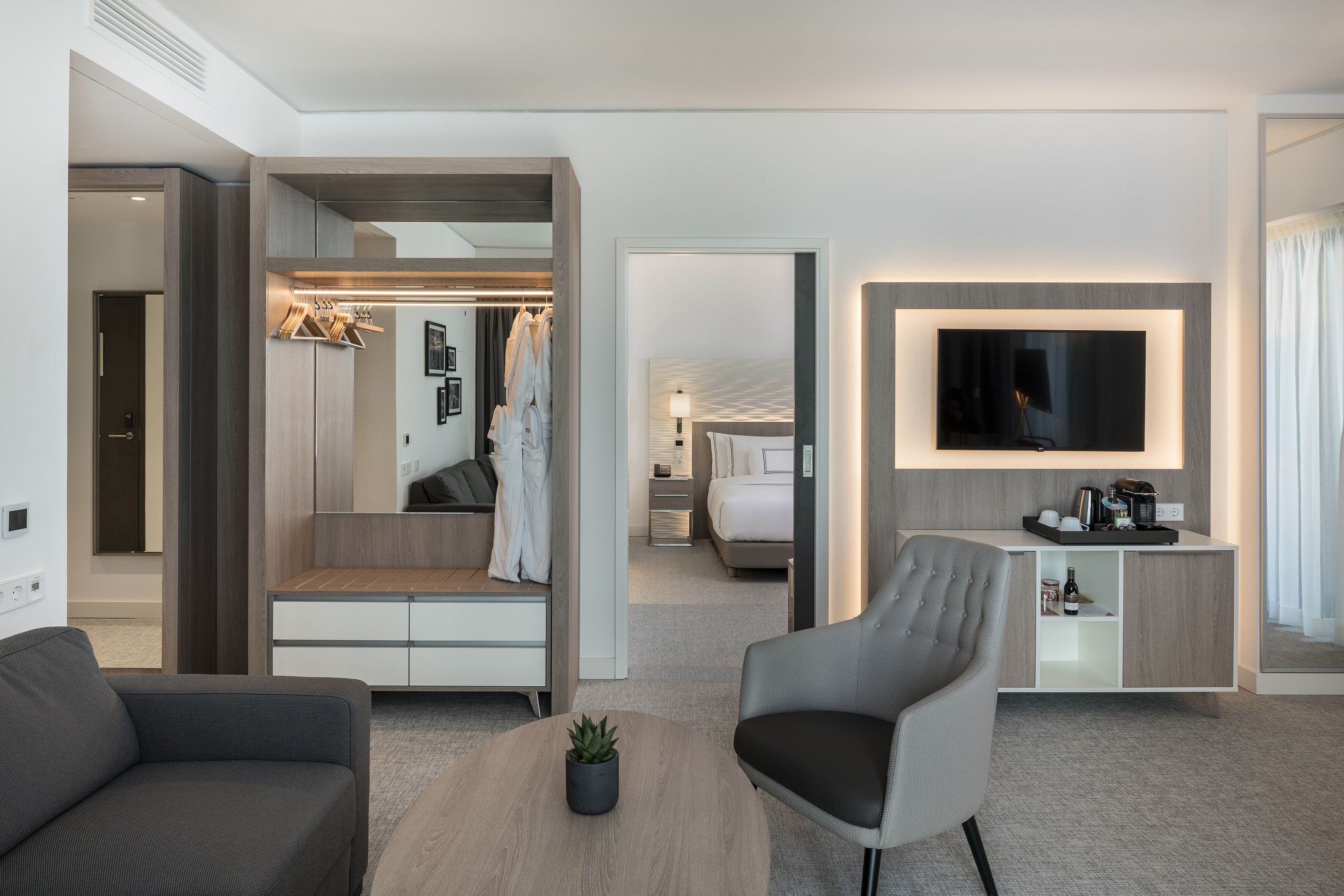 Ett modernt hotellrum med en sittgrupp, en TV, en minibar och en rymlig klädkammare.