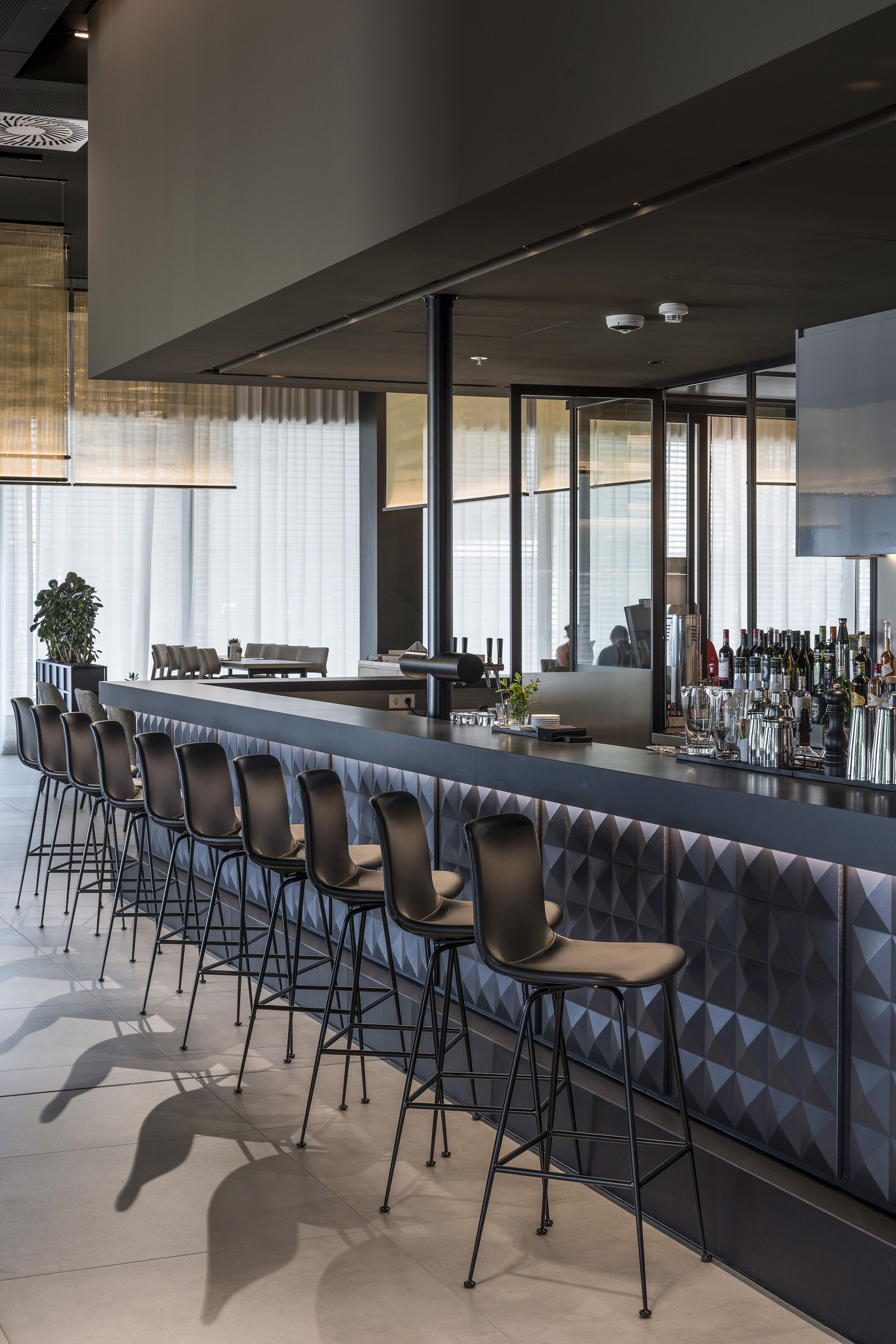 Un espace bar moderne doté d’un long comptoir, de nombreux tabourets et d’une grande variété de bouteilles.