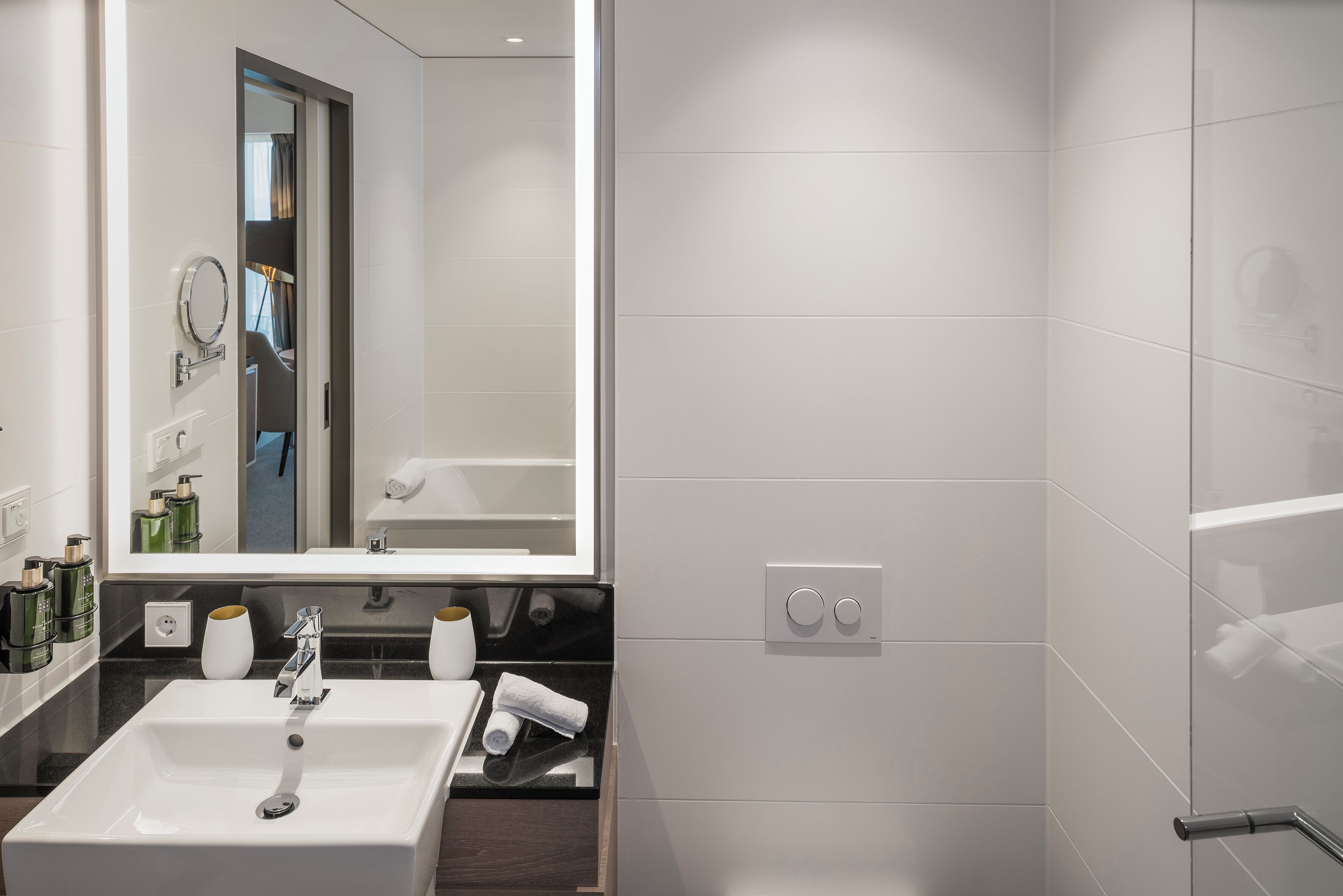 Ein modernes Badezimmer mit großem Spiegel, weißem Waschbecken und Handtuchhalter.