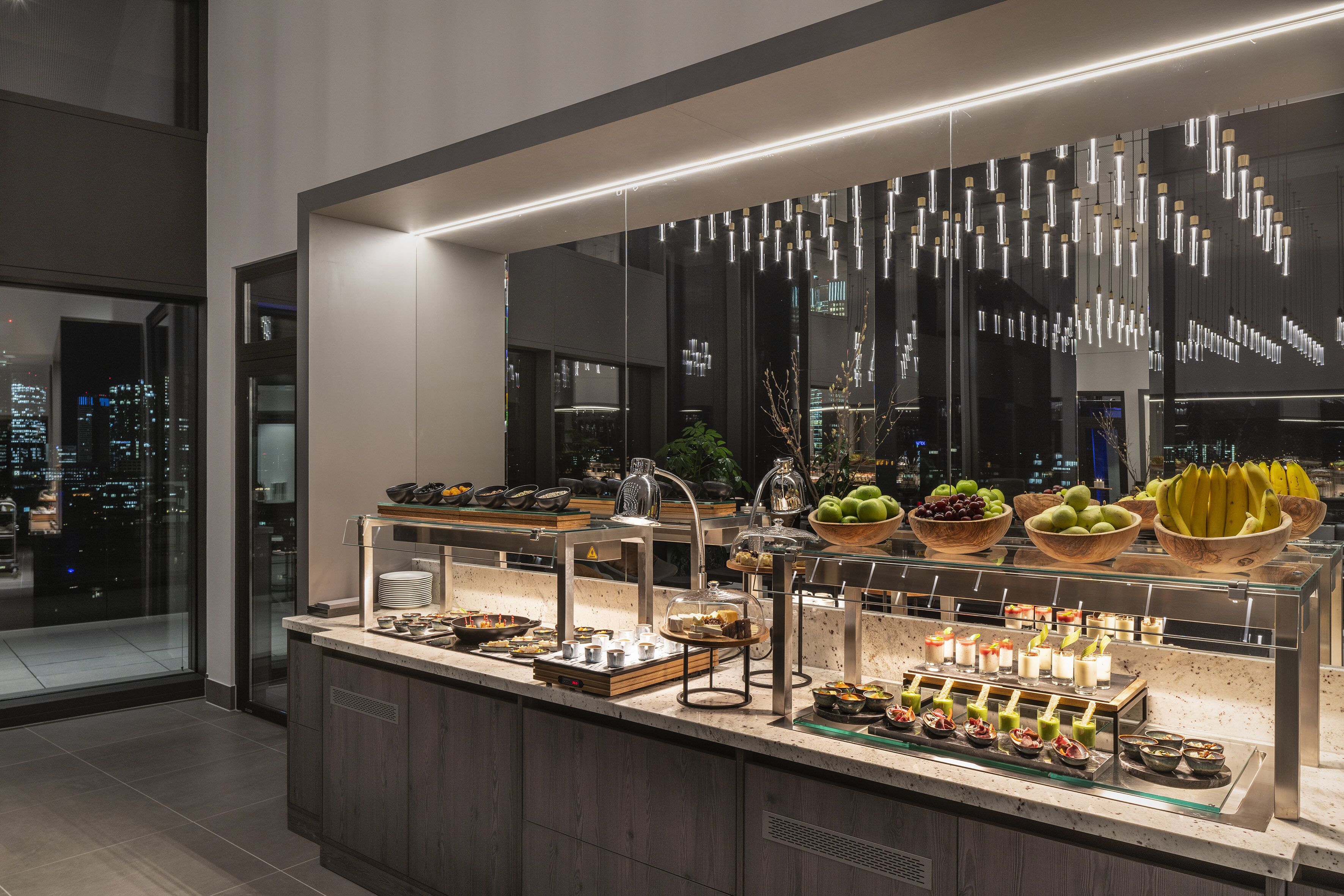 Ein reichhaltiges Buffet mit verschiedenen Speisen und Blick auf die Stadt durch große Fenster.