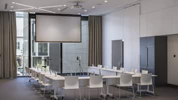 A conference room with a large screen, white tables, and chairs.