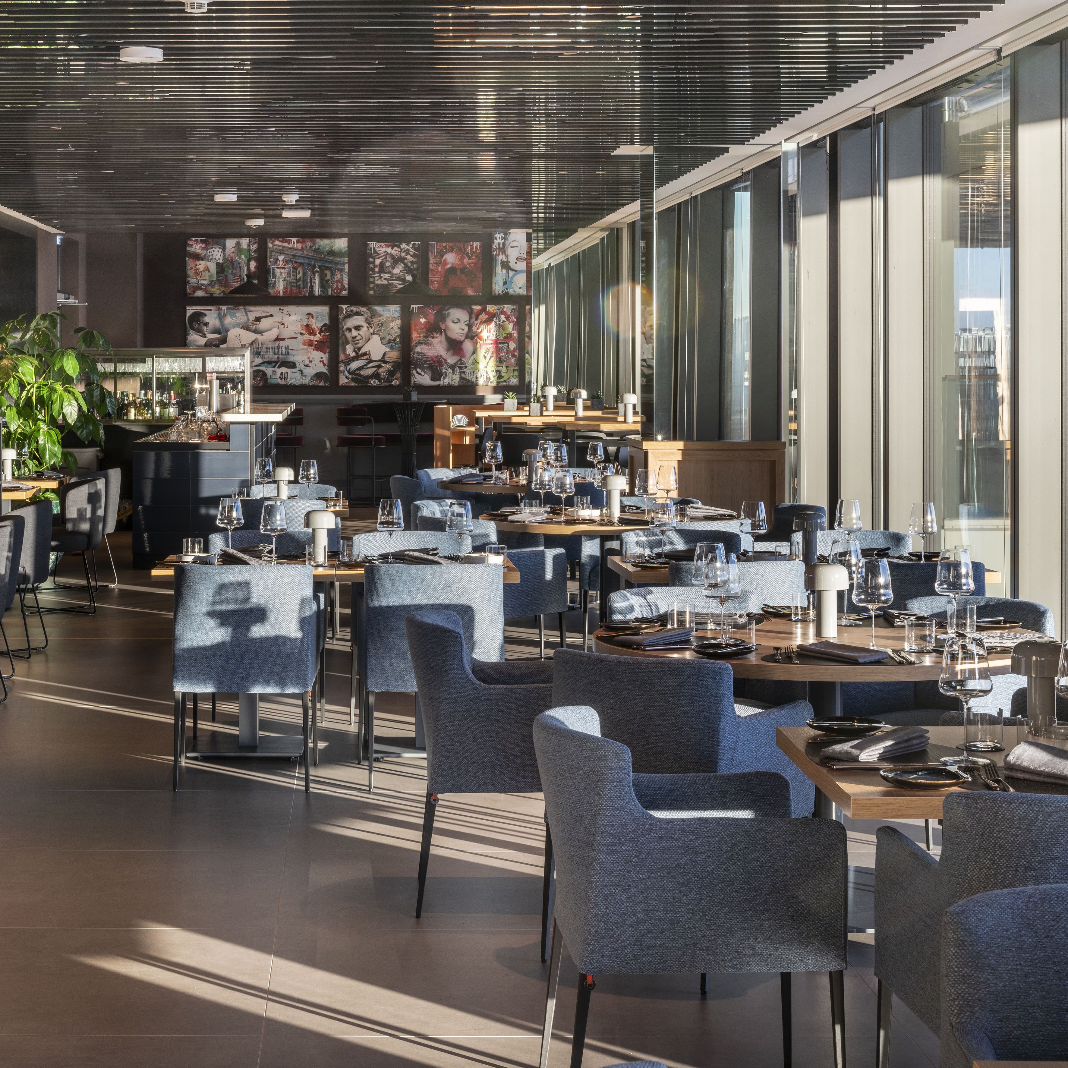 Een modern restaurant met meerdere eettafels en stoelen, grote ramen en kunst aan de muur.