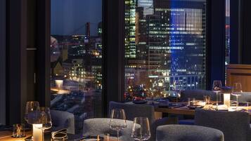 Un restaurant amb vista a la ciutat, mobiliari modern i una zona de menjador ben il·luminada.