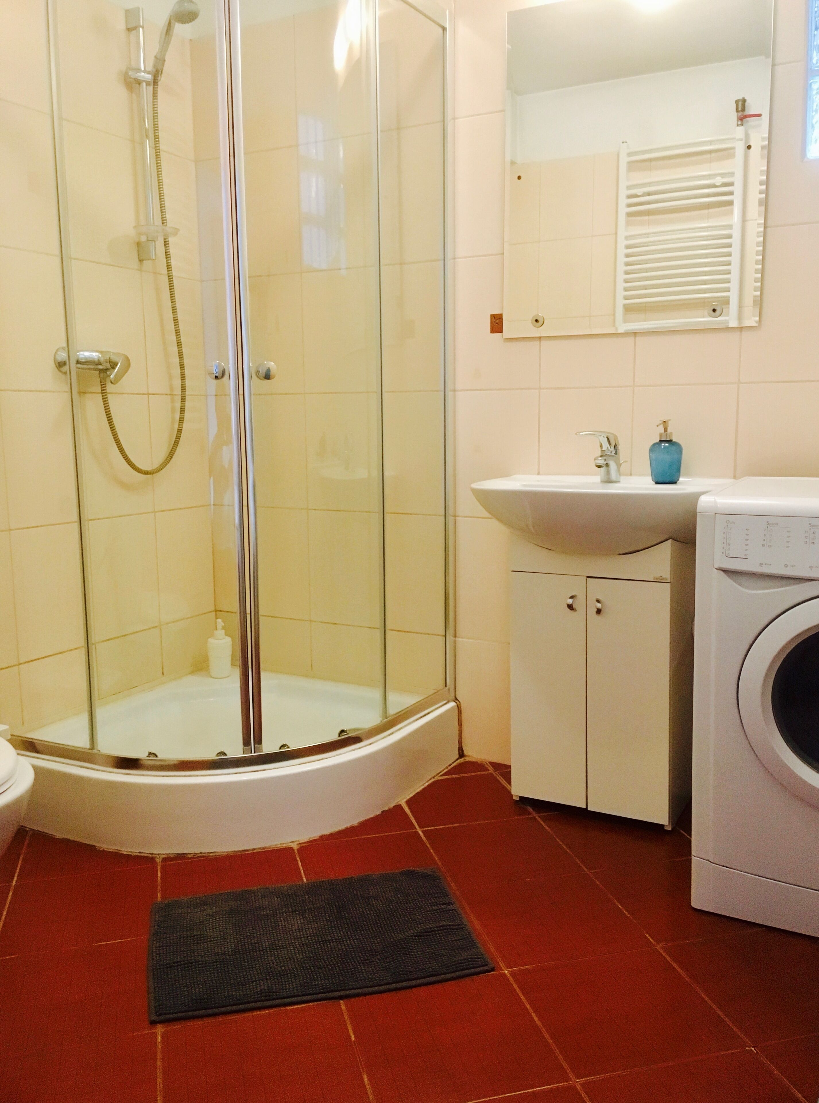 A bathroom with a glass-enclosed shower, a sink, a mirror, and a washing machine.