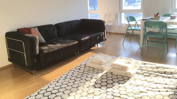Una sala de estar moderna con un sofá de cuero negro, un tapete estampado y un comedor con mesa y sillas.