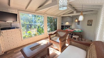 Una habitación con televisión, muebles de mimbre, una mesa de comedor y vistas a zonas verdes.