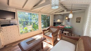 Una habitación con televisión, muebles de mimbre, una mesa de comedor y vistas a zonas verdes.