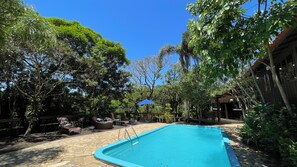A swimming pool surrounded by stone flooring, with outdoor furniture and a wooden structure in the background.