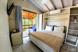 Un dormitorio con cama, un refrigerador pequeño, televisión y puerta corrediza de vidrio que da a un espacio al aire libre.