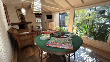 Una habitación con una mesa verde, un juego de la Oca y un televisor en la pared.