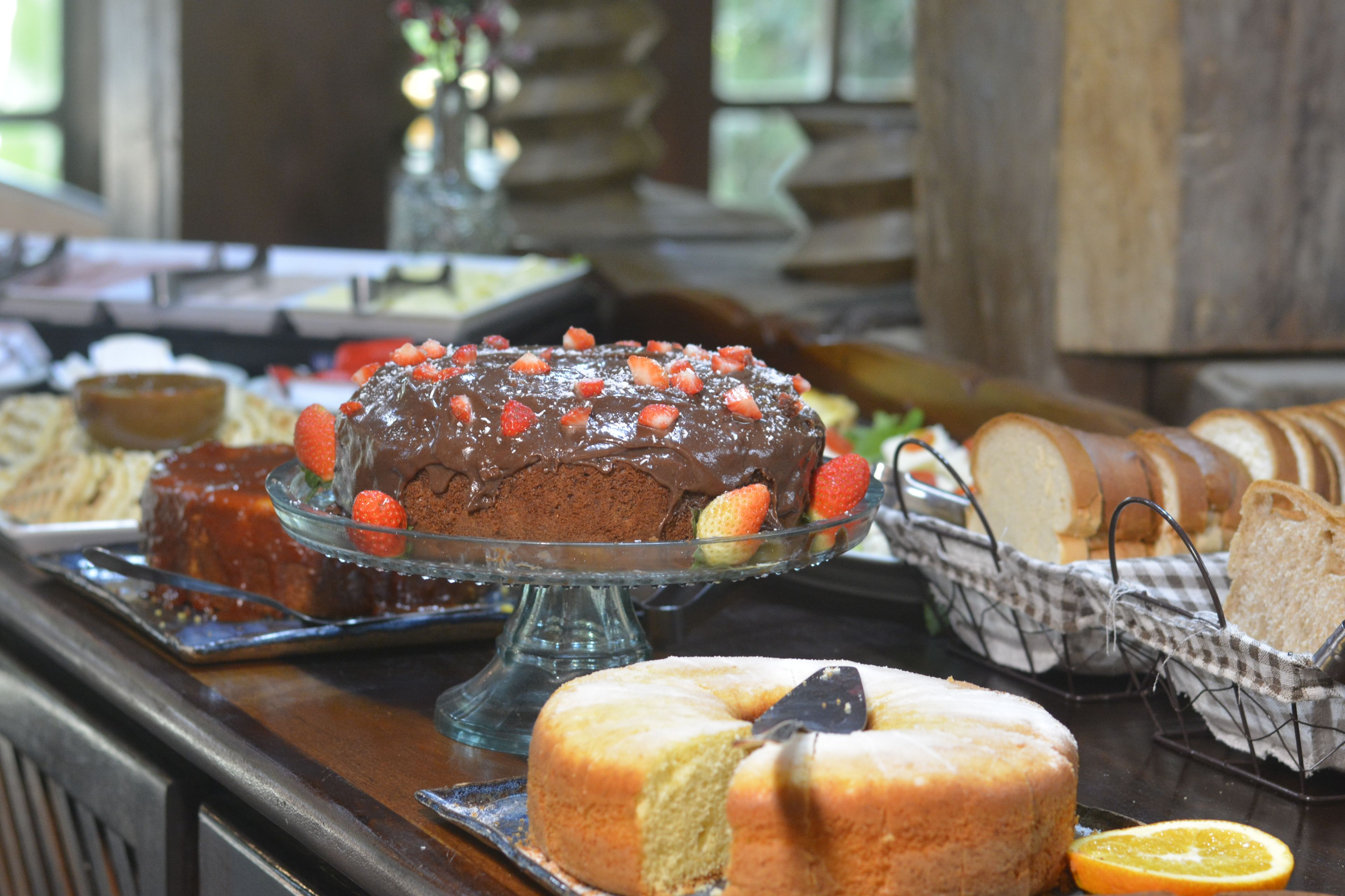 A buffet with various food items including a chocolate cake topped with strawberries, bread, and a fruit slice.