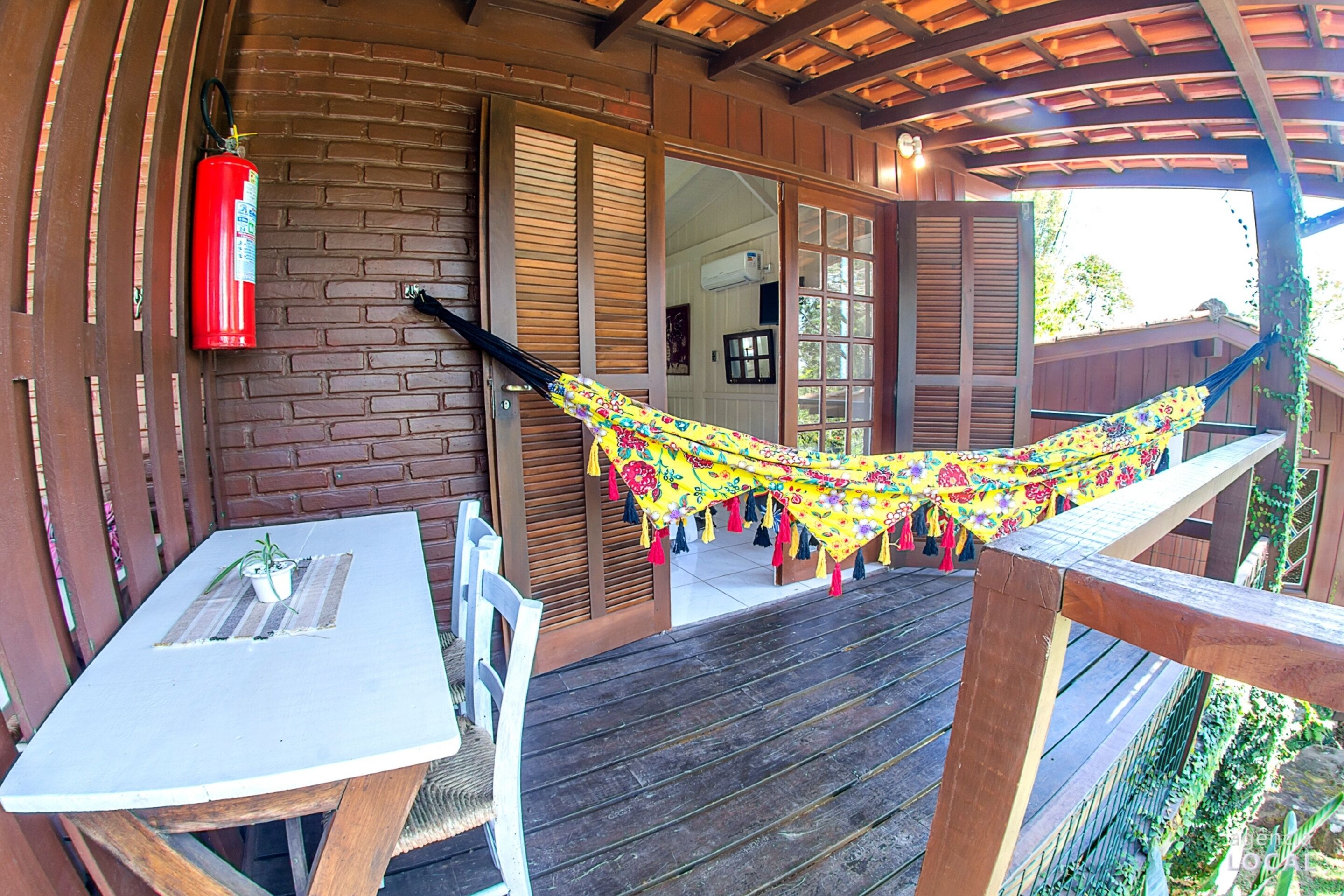 Eine Holzterrasse mit einer Hängematte, einem Tisch mit einem Blumentopf und einem roten Feuerlöscher.