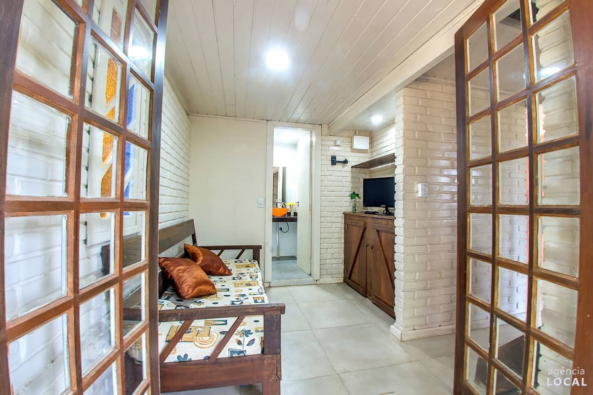A narrow hallway with a bed, a wooden cabinet, and a television on a stand.