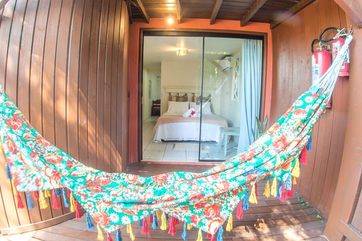A hammock on a wooden deck with a view of a bedroom through a glass door.
