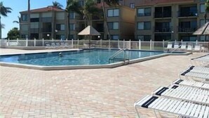 A swimming pool with lounge chairs, surrounded by a brick walkway and palm trees.
