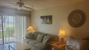 A living room with a sofa, a coffee table, a leather armchair, two lamps, and a wall clock.