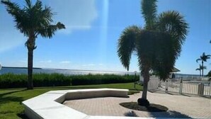 A landscaped area with palm trees, a curved white bench, and a view of the sea.