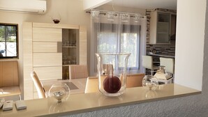 A modern kitchen with a dining area, featuring a glass vase on the counter, a dining table, and a kitchen island. - Detached house with terrace in the middle of a pine forest with sea view (Altea la vella)