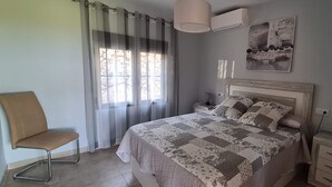 A bedroom with a bed, a chair, a bedside table, a nightstand, a wall-mounted air conditioner, and a window with curtains. - Detached house with terrace in the middle of a pine forest with sea view (Altea la vella)