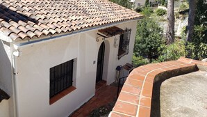A white building with a tiled roof, a small window with a metal gate, and a curved stone wall. - Detached house with terrace in the middle of a pine forest with sea view (Altea la vella)