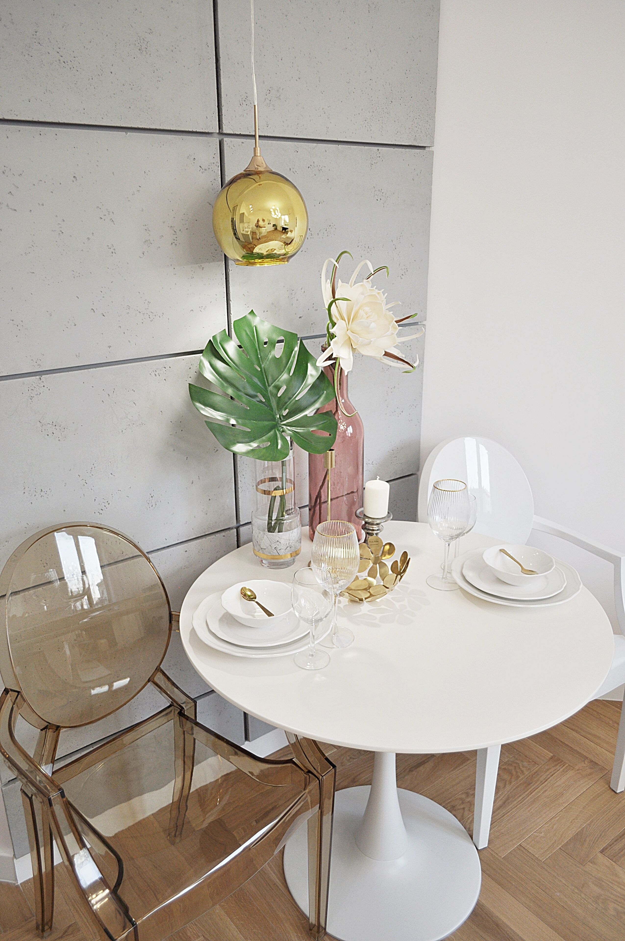 A dining table set with white plates, gold cutlery, and a vase with white flowers.