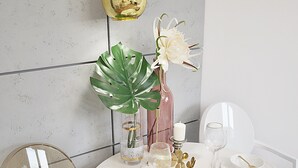 A dining table set with white plates, gold cutlery, and a vase with white flowers.