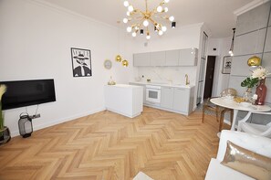 A modern living room with a flat-screen TV, a white sofa, and a dining area with a round table. - Apartament Superior-Aleja Wyzwolenia 3-5 (Warsaw)