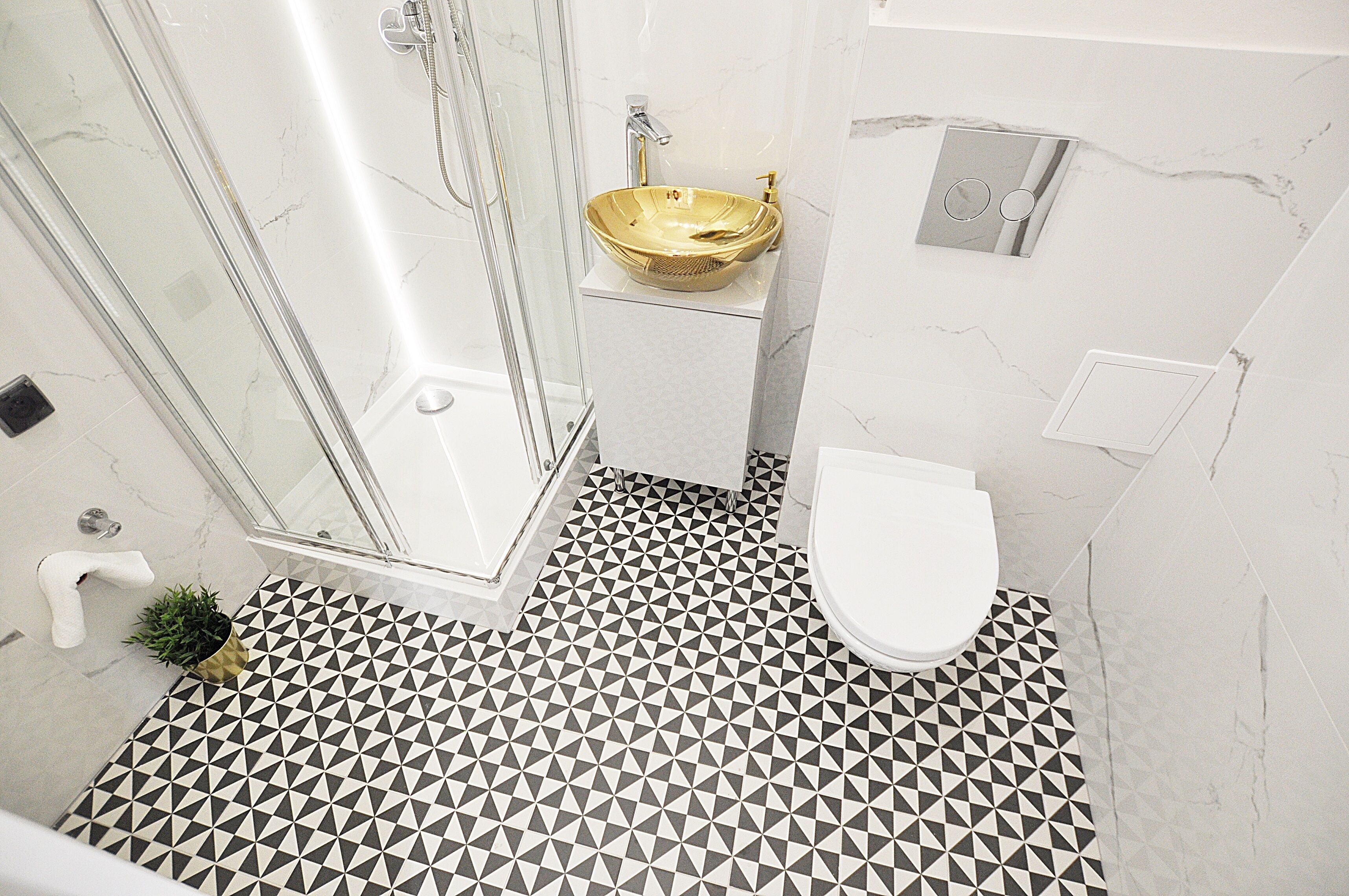A bathroom with a geometric patterned floor, a glass shower enclosure, a gold vessel sink, and a white toilet.