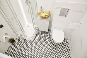 A bathroom with a geometric patterned floor, a glass shower enclosure, a gold vessel sink, and a white toilet. - Apartament Superior-Aleja Wyzwolenia 3-5 (Warsaw)