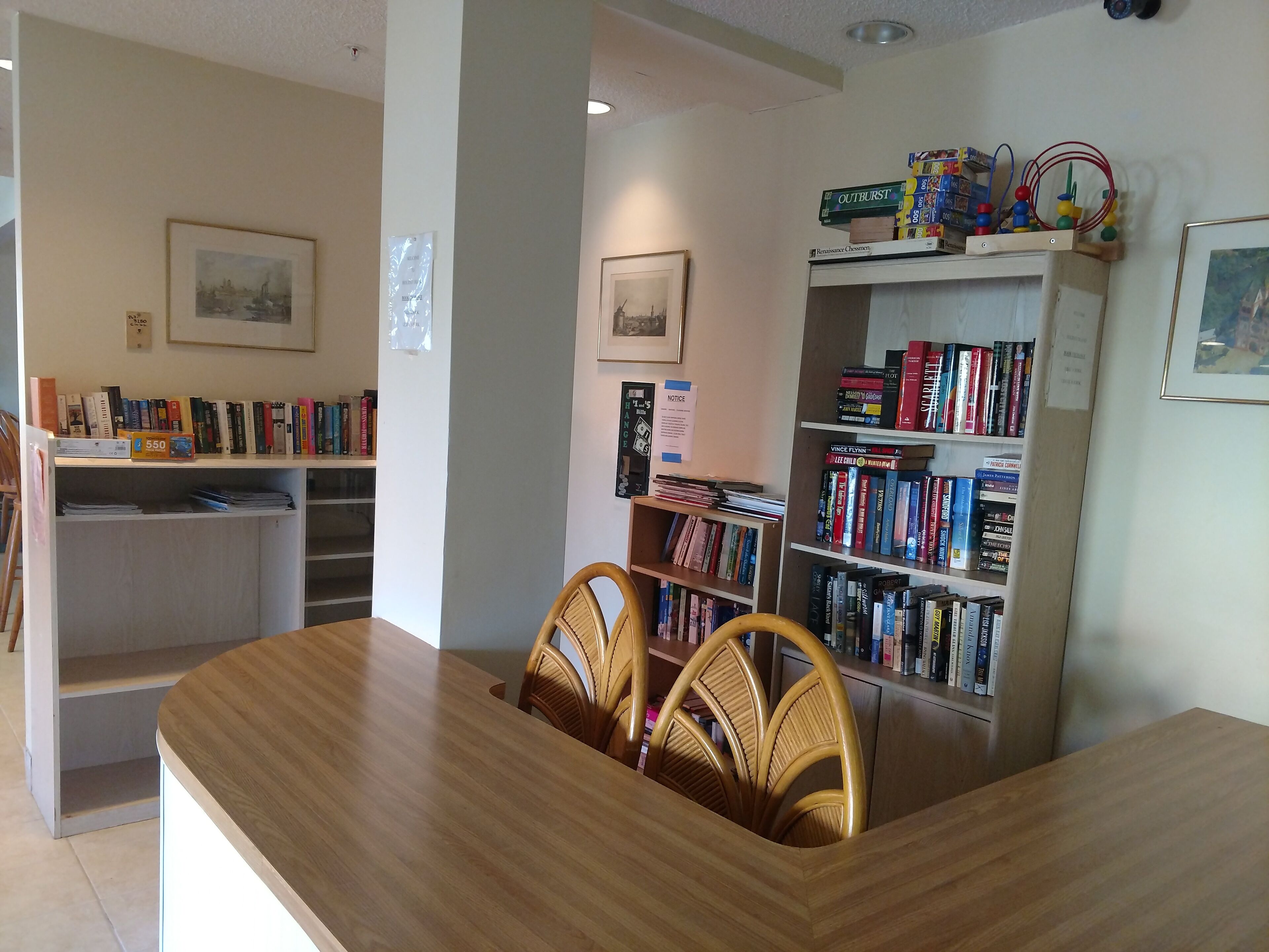 Una habitación con una mesa y sillas de madera, una estantería llena de libros y un cuadro en la pared.