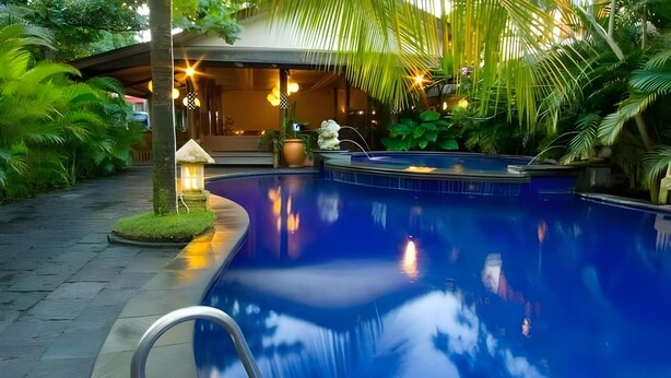 A serene indoor swimming pool with a clear view of the surrounding lush greenery and a well-lit lounge area. - Nyiur Indah Beach Hotel (Pangandaran)