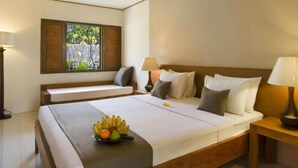 A hotel room with a large bed, bedside tables, a window with shutters, and a fruit bowl on the bed. - Nyiur Indah Beach Hotel (Pangandaran)