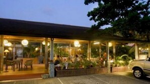An outdoor restaurant with tables and chairs, surrounded by plants and a car parked nearby. - Nyiur Indah Beach Hotel (Pangandaran)