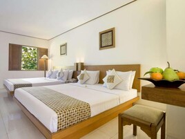 Habitación de hotel con dos camas, un escritorio con fruta y una ventana con vistas a zonas verdes.
