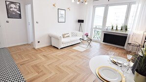 A modern living room with a white sofa, a dining table set for four, and a large window with a view of the city. - Apartamenty - ul. Marszałkowska 85 (Warsaw)